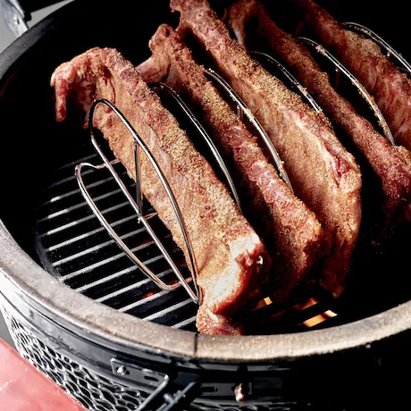 Grill mit mehreren Spareribs in einem Halter auf einem Grillrost